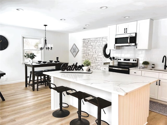 kitchen with a kitchen island, light wood-style flooring, a sink, stainless steel appliances, and tasteful backsplash