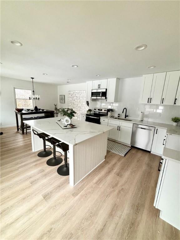 kitchen with light wood-style flooring, decorative backsplash, white cabinets, appliances with stainless steel finishes, and a center island