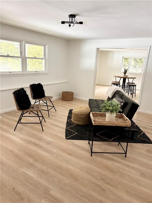 living area with baseboards, plenty of natural light, an inviting chandelier, and light wood-style flooring