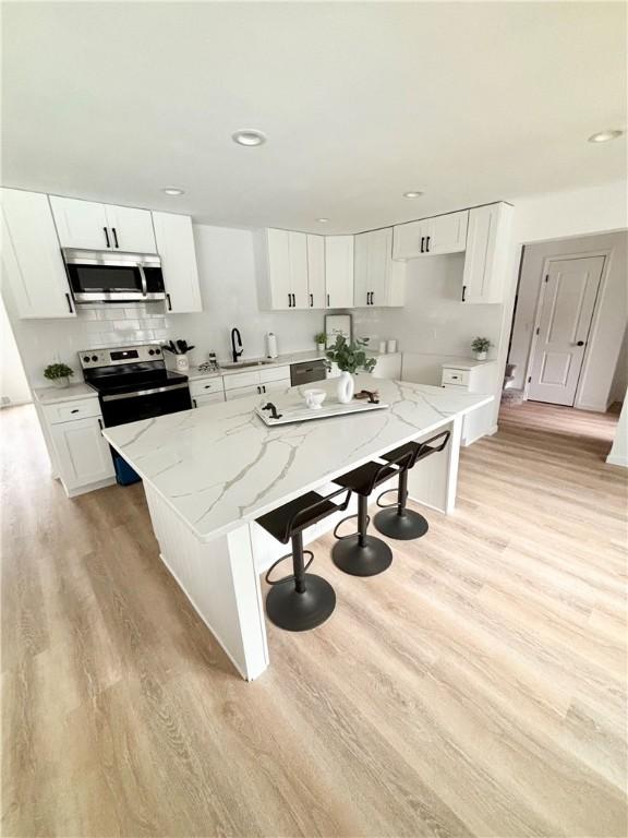 kitchen with a kitchen island, light wood-style flooring, a sink, stainless steel appliances, and a kitchen bar