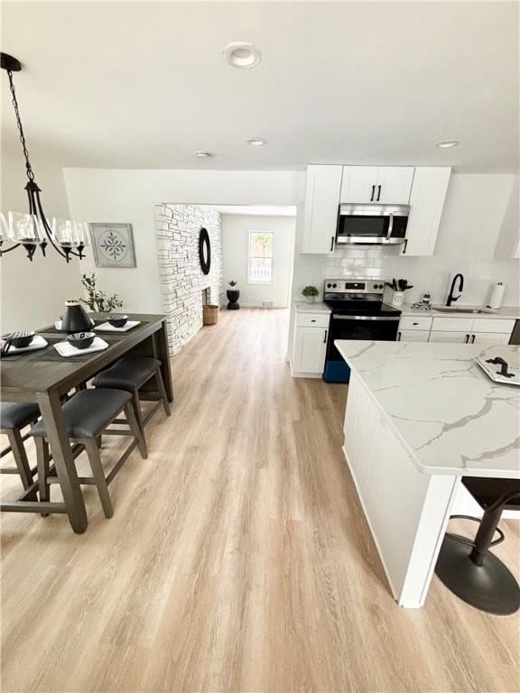 kitchen featuring light wood-type flooring, light stone counters, appliances with stainless steel finishes, a notable chandelier, and white cabinetry