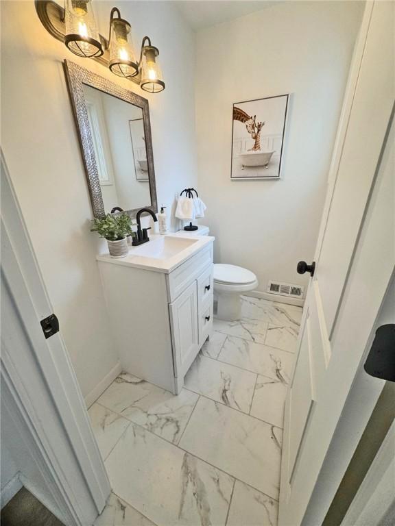 half bathroom featuring vanity, visible vents, baseboards, toilet, and marble finish floor