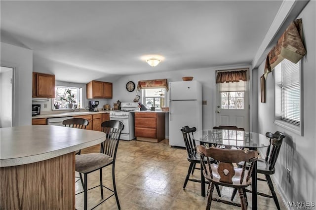 kitchen with light countertops, a kitchen bar, brown cabinetry, white appliances, and a sink