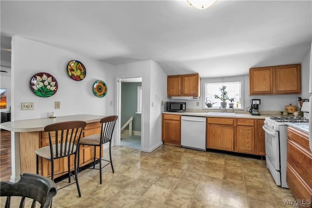 kitchen with white appliances, a sink, light countertops, a kitchen breakfast bar, and brown cabinets