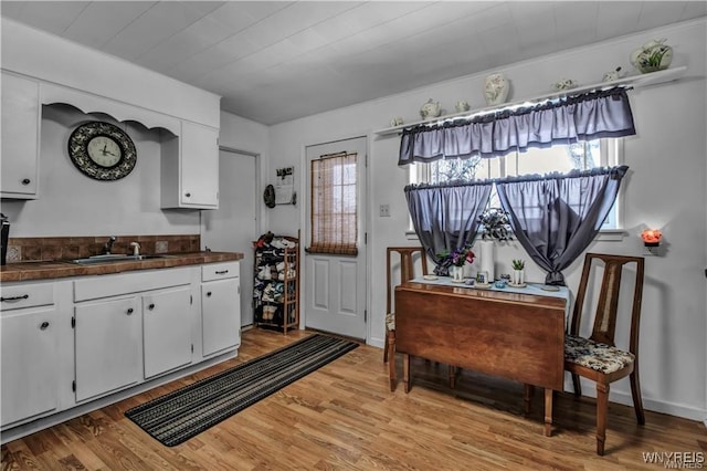 kitchen featuring a sink, light wood-type flooring, dark countertops, and white cabinets