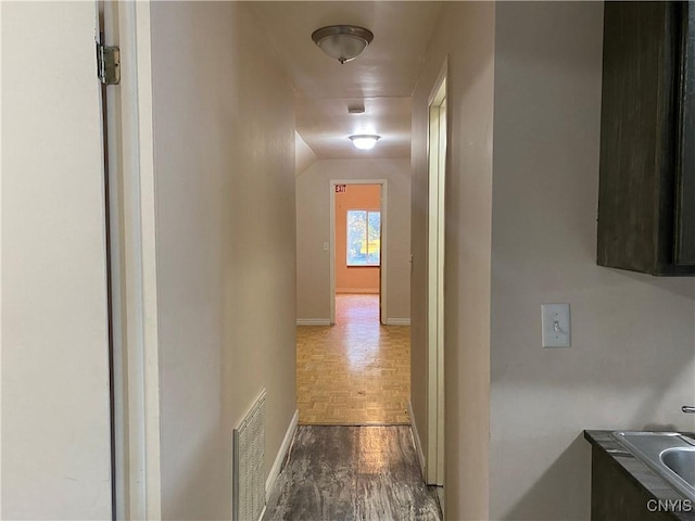 hallway featuring parquet flooring, visible vents, and baseboards