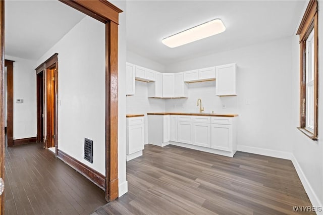 kitchen with visible vents, baseboards, dark wood finished floors, white cabinets, and a sink