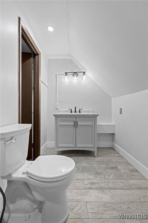 bathroom with baseboards, toilet, vanity, and lofted ceiling