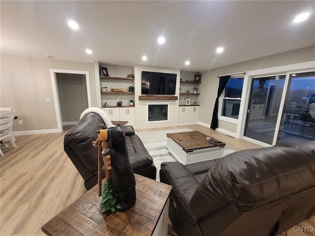 living room with recessed lighting, a large fireplace, baseboards, and light wood-style floors