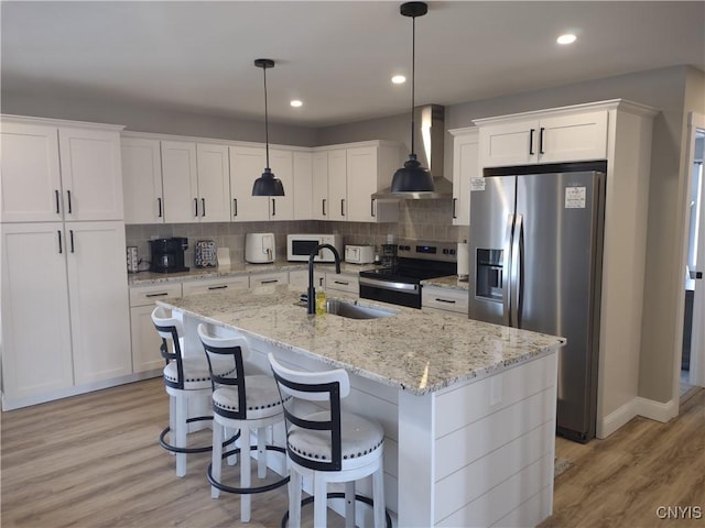 kitchen featuring light wood-style flooring, a sink, white cabinets, appliances with stainless steel finishes, and wall chimney range hood