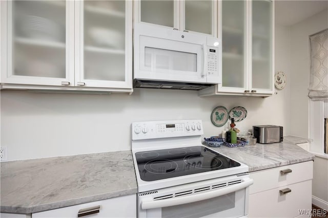 kitchen with white cabinetry, white appliances, light stone counters, and glass insert cabinets