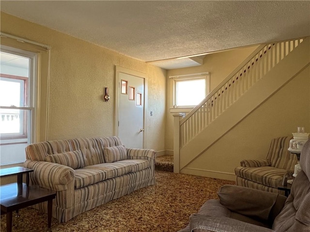 living area with a textured ceiling, carpet flooring, baseboards, stairs, and a textured wall