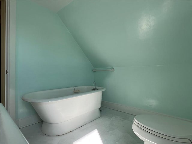 bathroom with vaulted ceiling, a freestanding tub, toilet, and baseboards