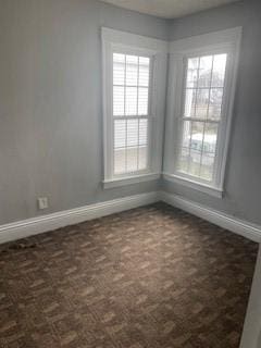 empty room featuring baseboards, dark colored carpet, and a wealth of natural light