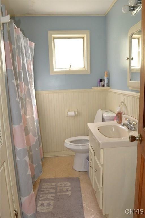 bathroom featuring wainscoting, toilet, vanity, and a shower with curtain