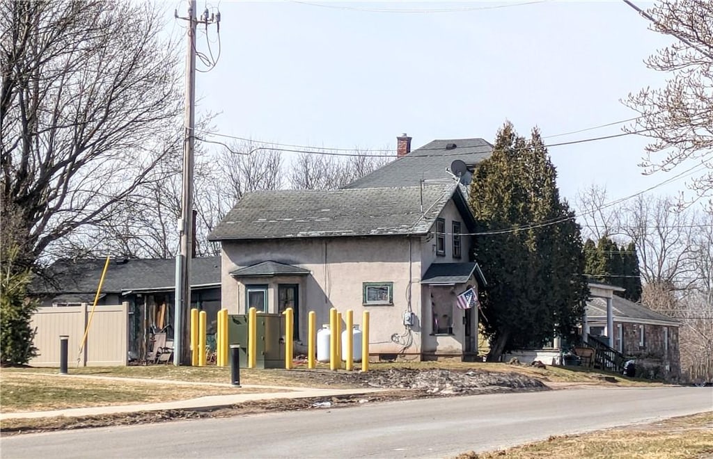 view of front of home featuring a shingled roof, stucco siding, a chimney, and fence