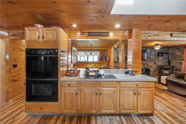 kitchen featuring black appliances, wood finished floors, open floor plan, a peninsula, and a wood stove