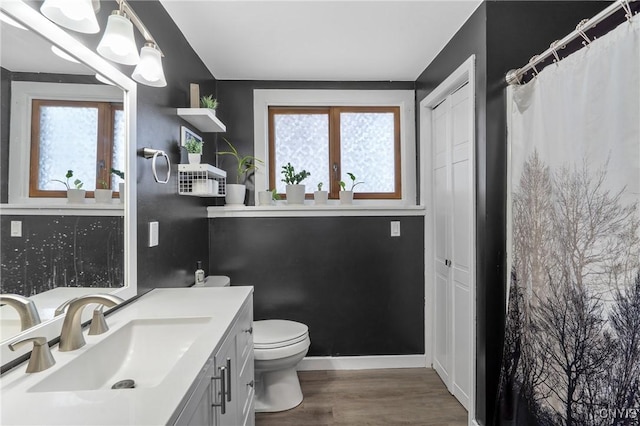 full bath with toilet, vanity, plenty of natural light, and wood finished floors