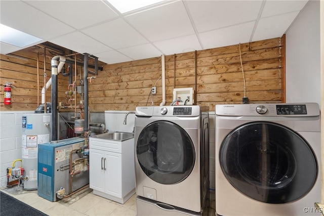 laundry room featuring wooden walls, cabinet space, water heater, a sink, and washing machine and dryer