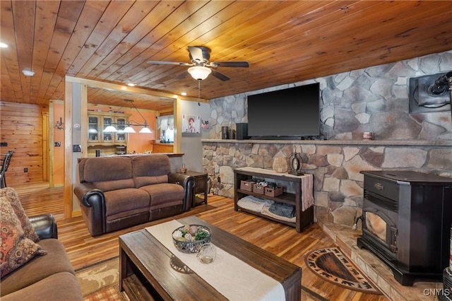 living room featuring wooden ceiling, a wood stove, ceiling fan, and wood finished floors