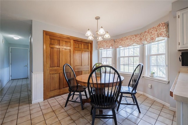 dining space with light tile patterned flooring, a wainscoted wall, and an inviting chandelier