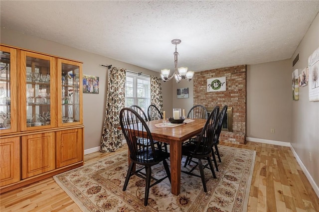 dining area with visible vents, baseboards, light wood-style flooring, an inviting chandelier, and a textured ceiling