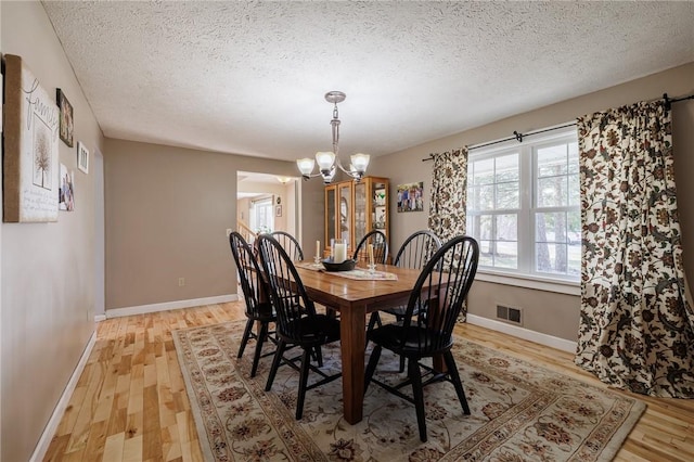 dining room with a notable chandelier, visible vents, light wood finished floors, and baseboards