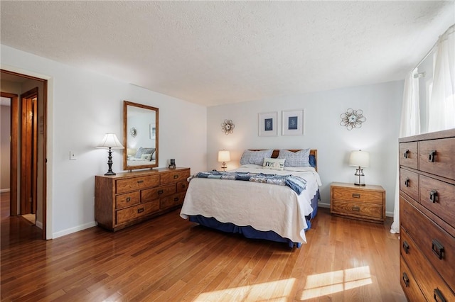 bedroom featuring a textured ceiling, baseboards, and wood finished floors