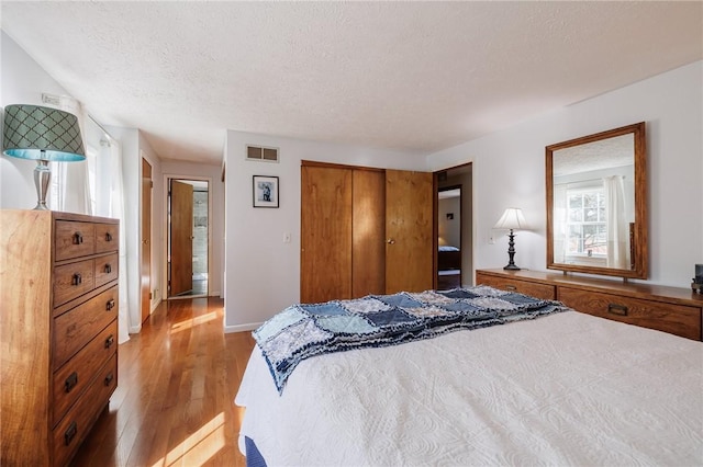 bedroom with baseboards, visible vents, light wood-style flooring, a closet, and a textured ceiling