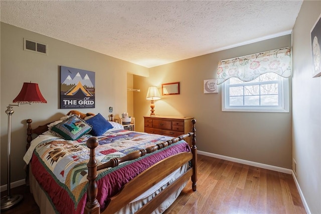 bedroom featuring visible vents, a textured ceiling, baseboards, and wood-type flooring