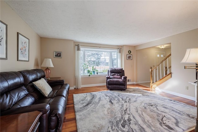 living area featuring stairway, wood finished floors, baseboards, and a textured ceiling