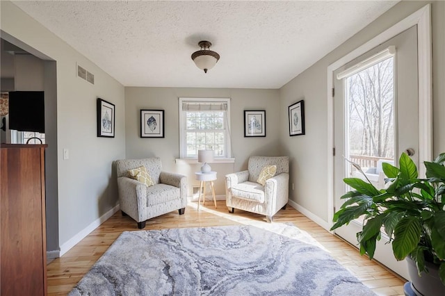 living area featuring a healthy amount of sunlight, visible vents, light wood finished floors, and a textured ceiling