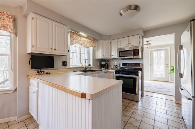 kitchen with a sink, white cabinetry, stainless steel appliances, a peninsula, and light tile patterned flooring