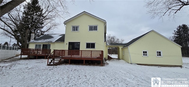 snow covered rear of property with fence and a wooden deck