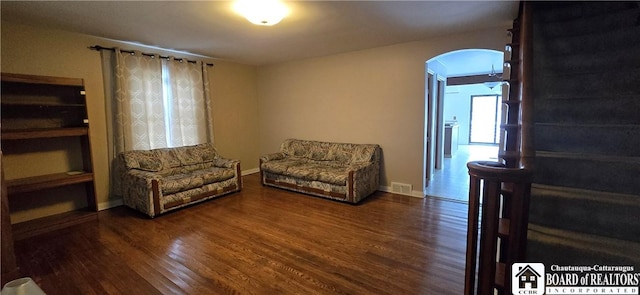 living room with visible vents, arched walkways, baseboards, and dark wood-style floors