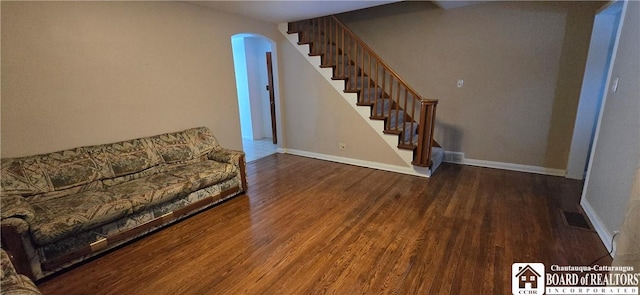 unfurnished living room featuring arched walkways, stairs, baseboards, and wood finished floors