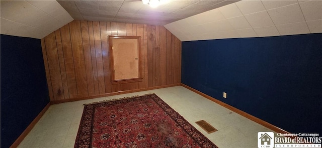 additional living space with visible vents, wooden walls, baseboards, lofted ceiling, and tile patterned floors