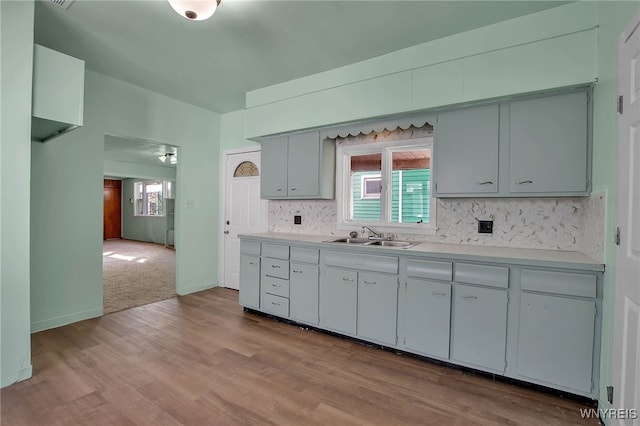 kitchen with a sink, decorative backsplash, light wood-style floors, and light countertops