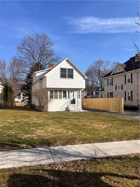 bungalow-style house with entry steps, a chimney, a front lawn, and fence