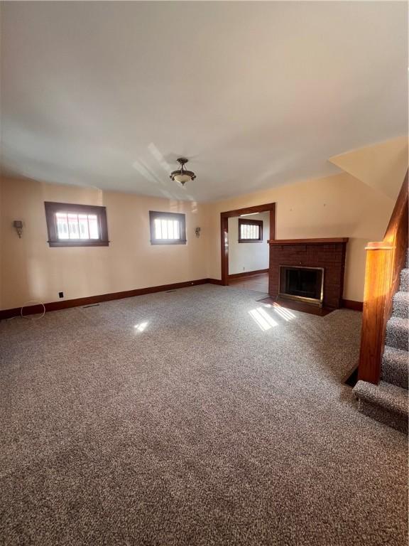 unfurnished living room with stairway, carpet flooring, a fireplace, and baseboards