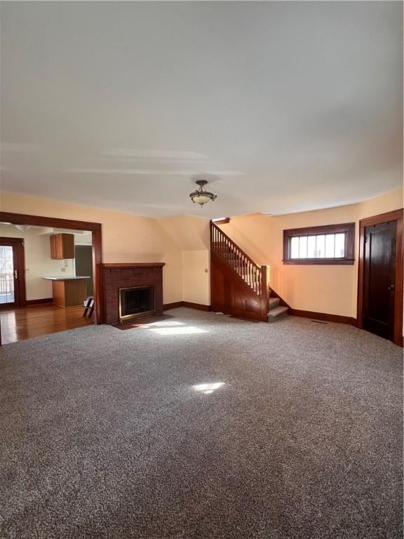 unfurnished living room featuring carpet flooring, a brick fireplace, stairs, and baseboards