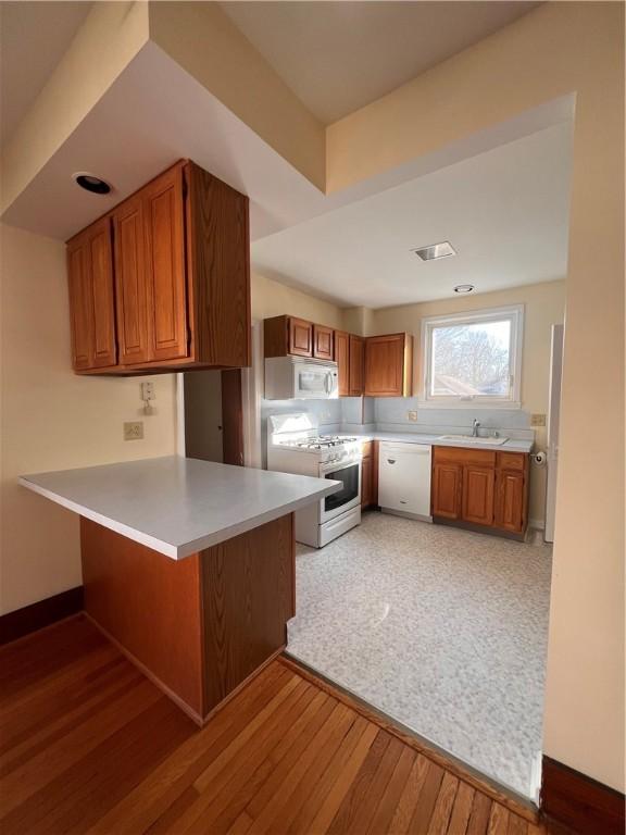 kitchen featuring brown cabinetry, white appliances, a peninsula, and a sink