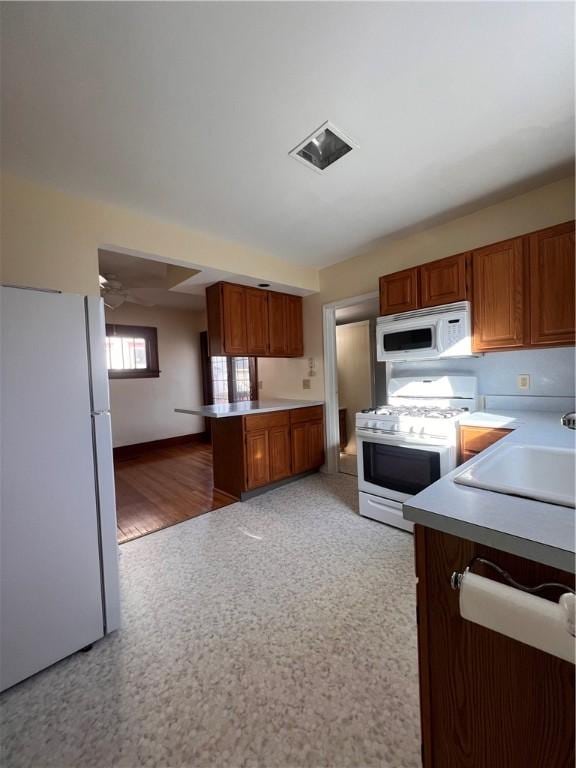 kitchen featuring a sink, visible vents, white appliances, and brown cabinetry