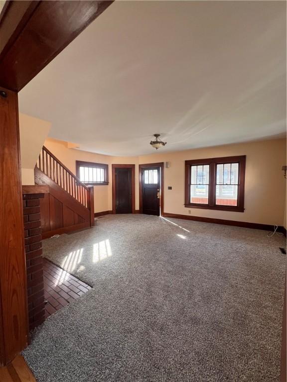 unfurnished living room featuring stairs, baseboards, and carpet floors