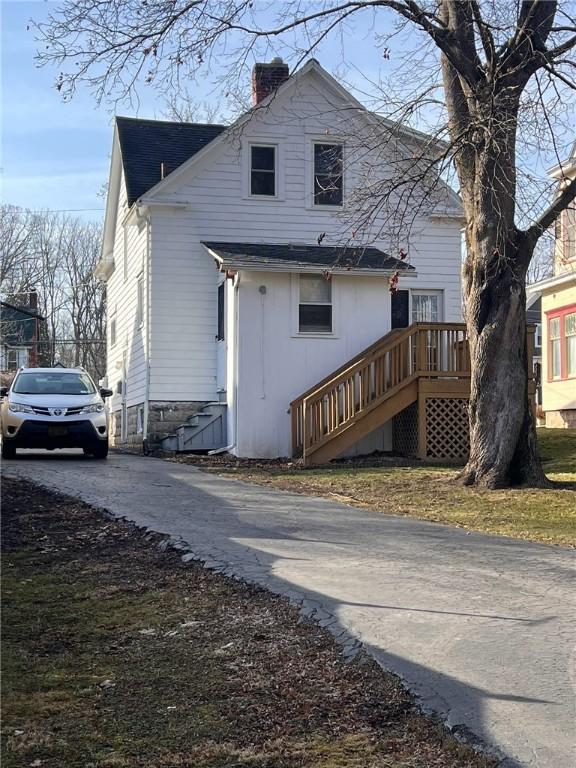 rear view of property with stairs, a shingled roof, driveway, and a chimney