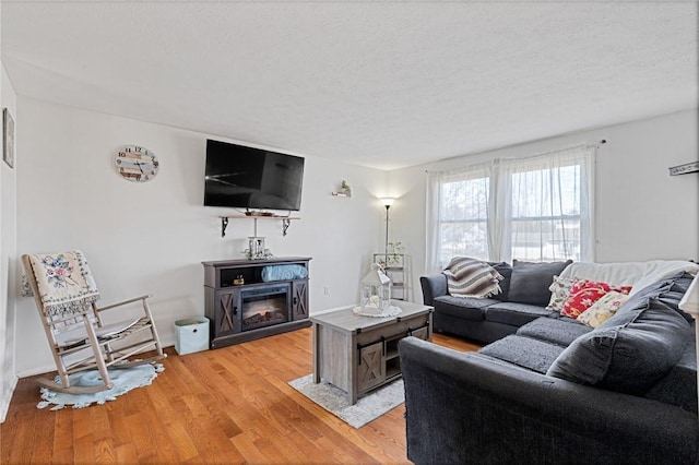 living area featuring baseboards, a textured ceiling, a glass covered fireplace, and light wood finished floors