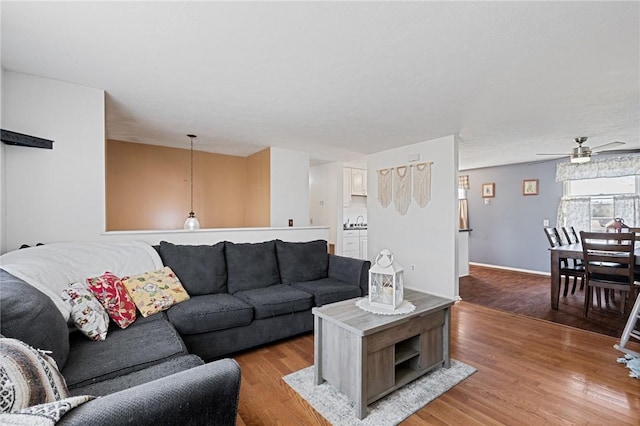 living room featuring baseboards, a ceiling fan, and light wood finished floors