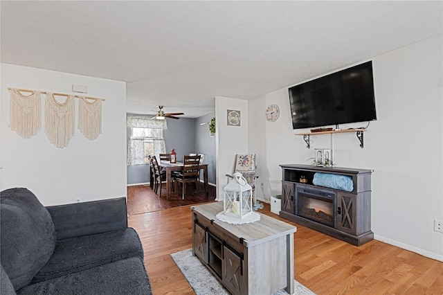 living area featuring ceiling fan, baseboards, and light wood-style flooring