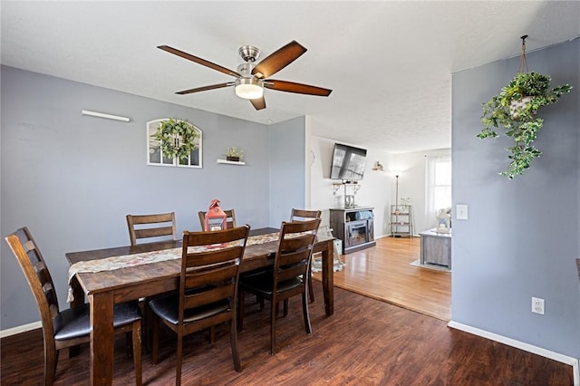 dining room featuring a ceiling fan, wood finished floors, baseboards, and a fireplace