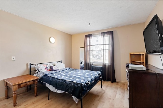 bedroom featuring baseboards, a textured ceiling, and light wood-style floors